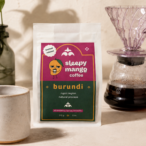 Sleepy Mango Coffee Burundi package on a beige surface with a plant and coffee maker in the background