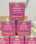 Stack of Cardamom Rose Chai tea tins with pink labels on a reflective surface.
